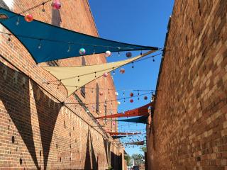 Alleyway with shade canopies and lights during day.
