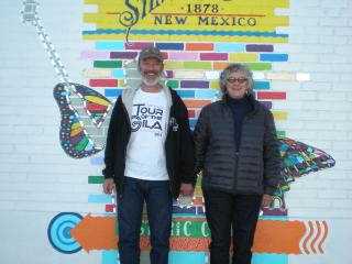 Two people standing by mural on brick wall.
