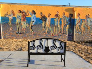Musical themed bench in front of mural of musicians.