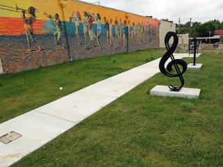 Musical note sculpture in front of mural of musicians with grass growing.