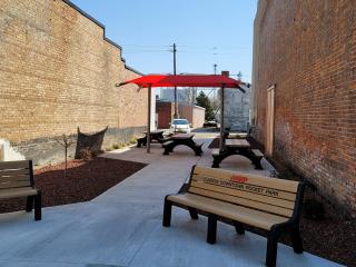Entrance to pocket park with benches, table, shade cover, landscaping.