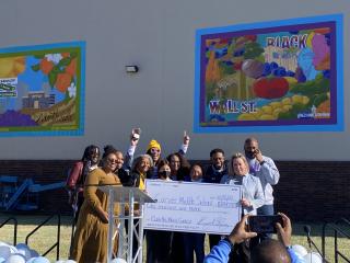 Large check presentation in front of mural.