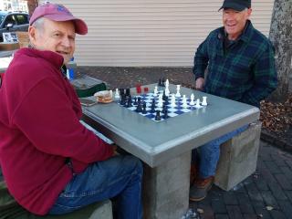 two men playing chess on outdoor game table.