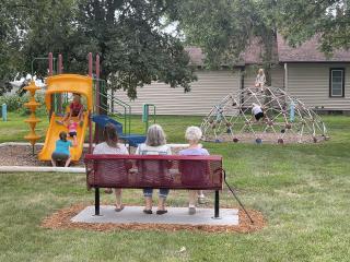 Three adults sitting on bench watching children at playground.