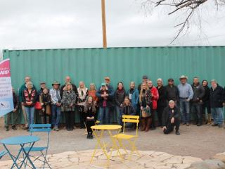 Group in front of shipping container with banner and cafe tables.