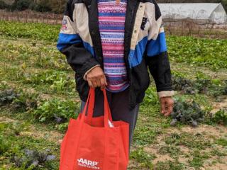 Older adult in garden with bag of produce.