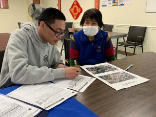 A staff member helps an elderly Chinese woman complete a community survey.