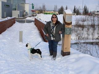 Woman walking dog next to trail markers in the snow.