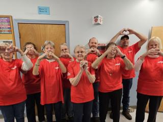 Group of volunteers making heart signs with fingers, standing near AED.