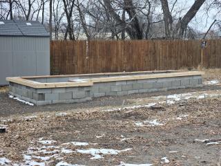 Raised garden bed of cinderblocks, with wooden seating along edge.