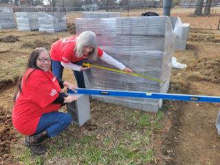 Two older adults leveling concrete blocks to create raised garden beds.