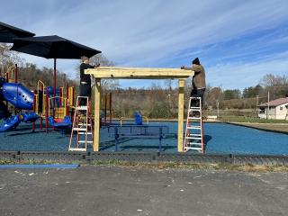 Installing wooden shade covering over bench at playground.