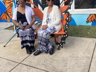 Two older women sitting on Monarch butterfly bench.