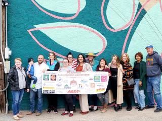Community members holding thank you sign in front of a mural.