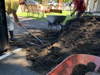 Volunteers filling wheelbarrow with soil.