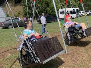 Two adults using wheelchair-friendly swings.