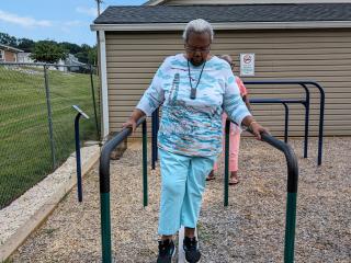 Older adult using outdoor balance beam with handrails.