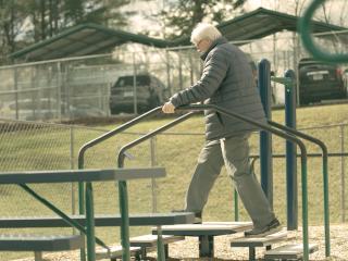 Older adult using outdoor stair exercise with handrails.