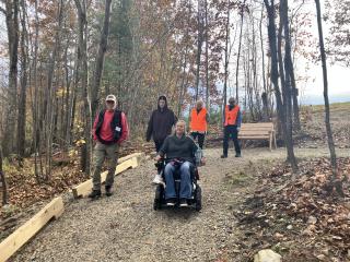 Wheelchair users on accessible trail, with new bench in background.