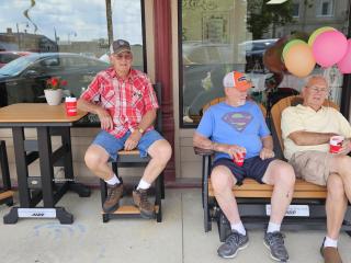 Older adults sitting in rocking chair bench and at table.