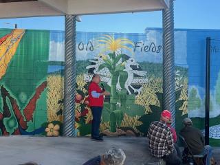 Native American artist explaining mural imagery at event.