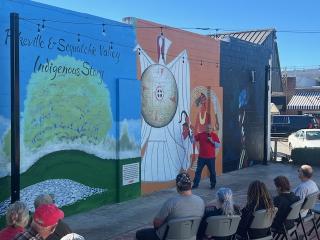 Native American artist explaining mural imagery at event.